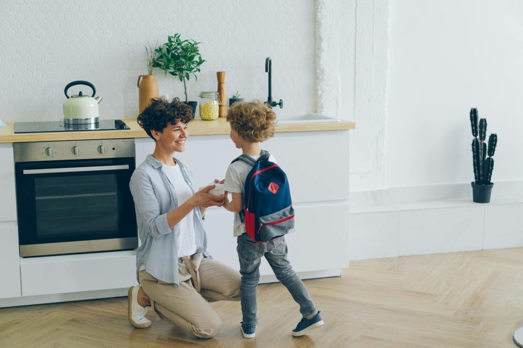 smiling mother and son with backpack in kitchen
